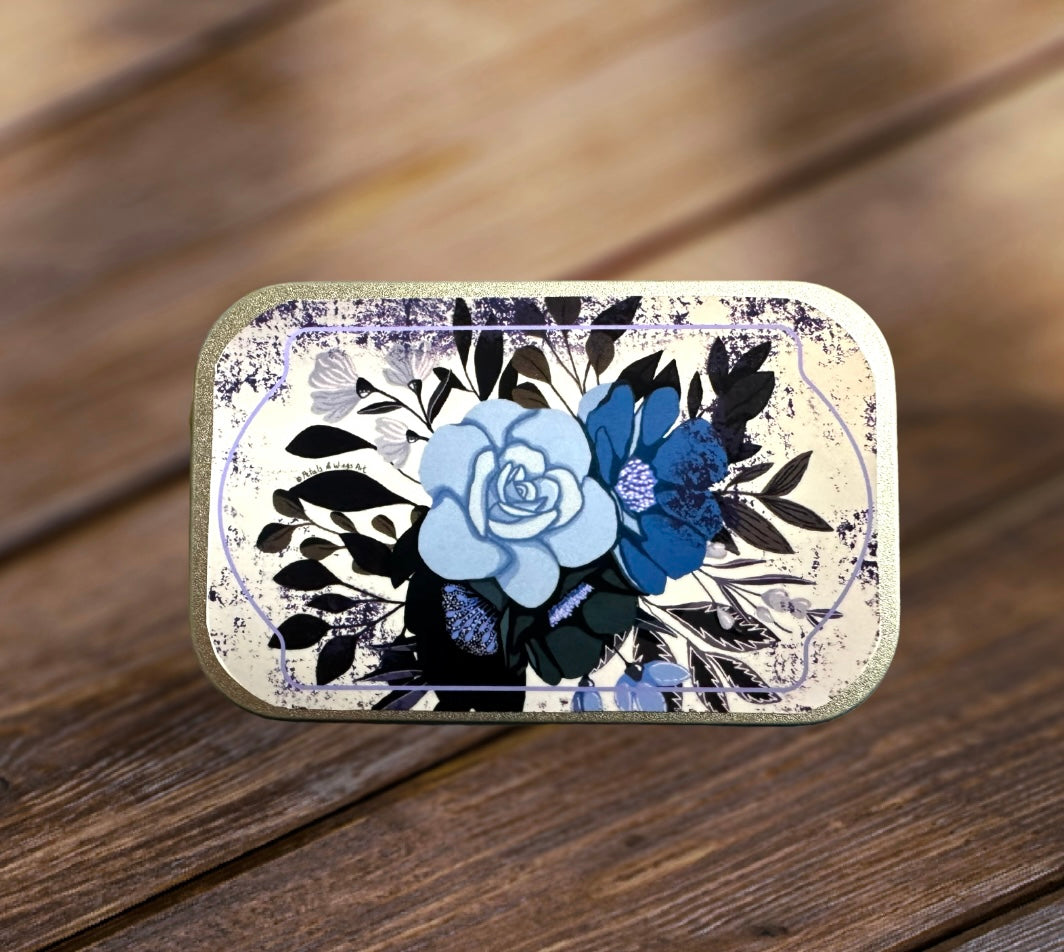 Metal rectangular aluminum tin decorated with a vintage look. Features 2 flowers blooming has an accent of purple color around the flowers. It the perfect hinged tin to keep your small trinkets, or candy, dog treats, etc. Measures 2.36 inches by 3.74 by 0.82 inches tall.